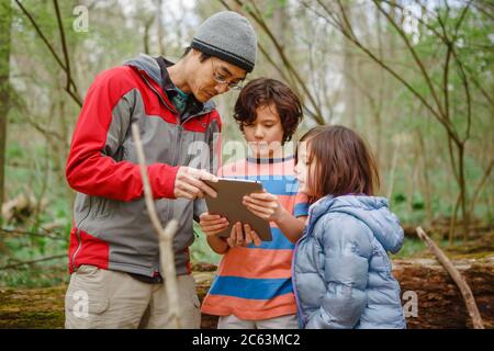 Ein Vater und Kinder betrachten ein Tablet auf einem Spaziergang durch den Wald Stockfoto