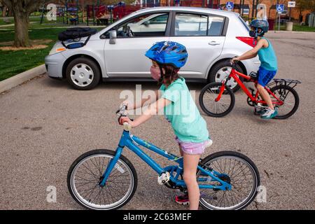 Ein Junge und ein Mädchen mit Gesichtsmasken fahren zusammen Fahrräder Auf einem Parkplatz Stockfoto