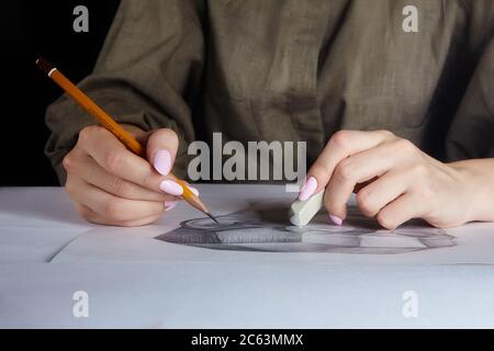 Die Hand des Künstlers hält einen Bleistift und Radiergummi aus der Nähe. Vor dem Hintergrund von Graffiti wird ein Porträt eines Mannes gezeichnet Stockfoto
