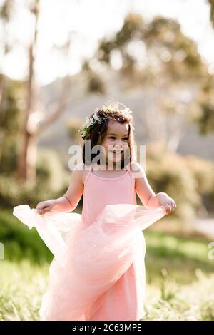 Junges Mädchen in Tutu und Blumenkrone im Feld stehend, lächelnd Stockfoto