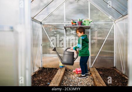 Kleiner Junge wässern Samen im Hinterhof Gewächshaus während der Frühlingszeit Stockfoto