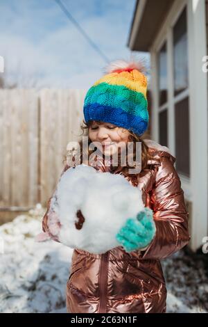 Junges Mädchen in Regenbogen Hut hält riesigen Schneeball im Winter Stockfoto