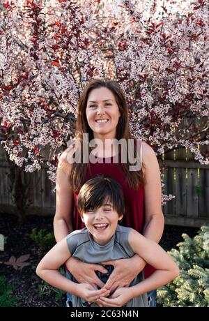 Mutter und kleiner Sohn umarmen sich vor blühenden Bäumen im Garten. Stockfoto