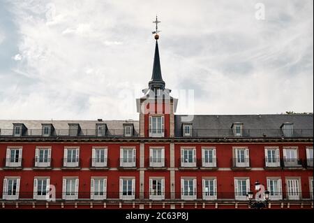 Niedriger Winkel des historischen Gebäudes Casa de la Panaderia mit roten Wänden und Kreuz auf hohen Turm gegen bewölkten Himmel auf der Plaza Mayor oder Hauptplatz in Stockfoto