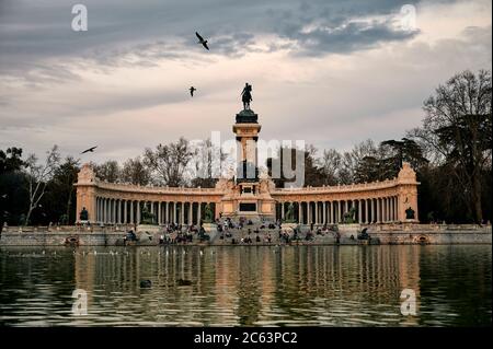 Reisende Menschen sitzen auf Stufen in der Nähe von altertüm Denkmal des Königs Alfonso XII in der Nähe Teich mit sauberem Wasser im Retiro Park in Madrid Stockfoto