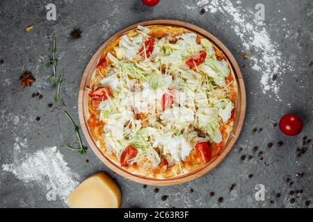 Leckere Pizza im Caesar-Stil mit weißer Sauce, Huhn, Parmesan, Ei, Kirschtomaten und frischem Salat auf Holzhintergrund Stockfoto