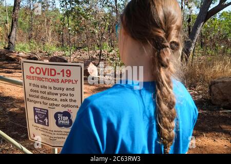 Ein Mädchen schaut auf ein Covid-19 Schild am Eingang des Litchfield National Park im Northern Territory in Australien Stockfoto