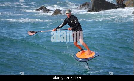 Älterer Mann, der fit bleibt, indem er Spaß auf dem Tragflügelboot hat, steht auf dem Paddle Board Stockfoto