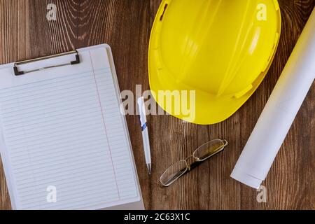 Architekt oder Ingenieur arbeiten an Blaupause Architektur-Modus im Büro Notizblock Konstruktion auf gelben Schutzhelm auf Holzhintergrund. Stockfoto