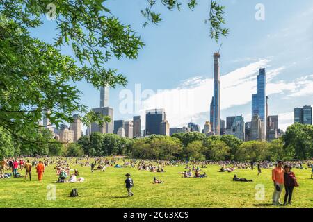 New York City/USA - 25. Mai 2019 Menschen ruhen sich im Central Park aus, dem schönen Sonnentag in New York City. Manhattan Skyline, wie es aus dem Park Stockfoto