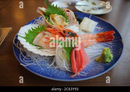 Garnelen, Schalentiere, Thunfisch, Schalentiere. Viele Meeresfrüchte werden zu Sashimi gemacht, die als japanische Mahlzeit auf einem blauen Teller serviert werden. Stockfoto