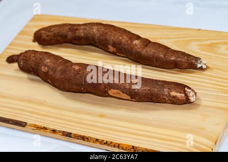 Rohe Yucca auf dem Holztisch, Manihot esculenta. (Cassava roh Knolle). Maniok, auch Mandioca, Yuca, Balinghoy, mogo, Mantoca, kamoteng kahoy genannt, Stockfoto