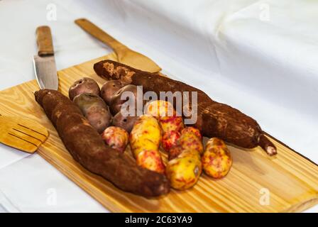 Rohe Yucca auf dem Holztisch, Manihot esculenta. (Cassava roh Knolle) mit regionalen Kartoffeln aus den Anden auf einem Markt in Peru, Bolivien, Argentinien, s Stockfoto