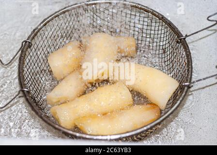 Waschen von Manihot mit Wasser in einem Metallsieb, Manihot esculenta. Maniok, auch Mandioca, Yuca, Balinghoy, mogo, Mantoca, kamoteng kahoy, Tap genannt Stockfoto