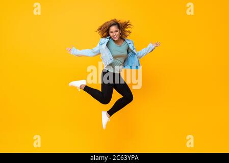 Glücklich energisch lächelnd junge afroamerikanische Frau springen isoliert auf gelbem Hintergrund Stockfoto