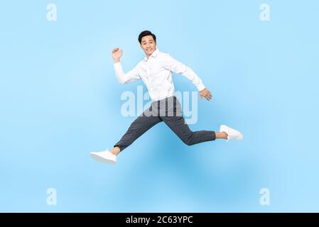 Glücklich lächelnd energetische asiatische Mann in semi formale Kleidung Springen in der Luft isoliert auf hellblauem Hintergrund Stockfoto