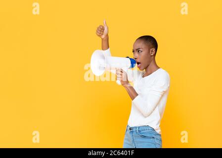 Afroamerikanische Frau, die auf Megaphon schreit und Daumen hoch gibt, isoliert auf gelbem Hintergrund Stockfoto