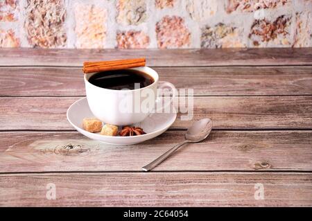 Auf einer Untertasse auf einem Holztisch steht eine Tasse schwarzen Kaffee mit Zimtanis und Scheiben braunem Rohrzucker. Nahaufnahme. Stockfoto