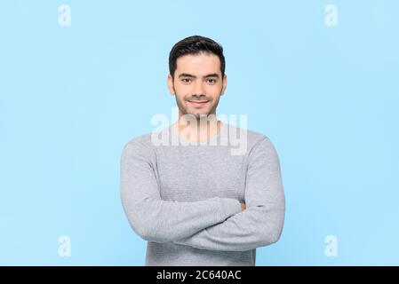 Porträt eines lächelnden freundlichen gutaussehenden Mannes in einfarbig grauem T-Shirt mit Armen, die isoliert in hellblauem Studiobakground gekreuzt sind Stockfoto