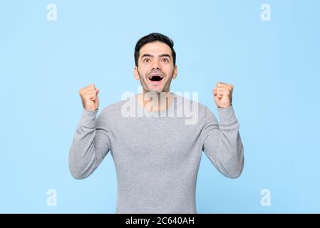 Aufgeregt überrascht Kaukasischen Mann seine Fäuste zusammenklemmend und Blick auf hellblauen Hintergrund isoliert Stockfoto