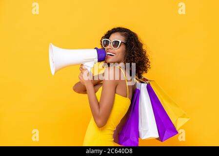 Glückliche schöne Frau mit Einkaufstaschen und Megaphon auf isolierten bunten gelben Hintergrund für Verkauf und Rabatt-Konzepte Stockfoto