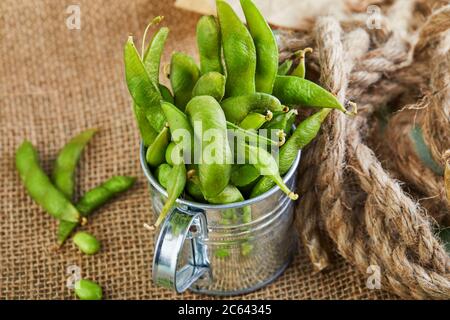 Edamame oder Sojabohnen in einem glänzenden Eimer auf einem braunen Sacktuch. Stockfoto