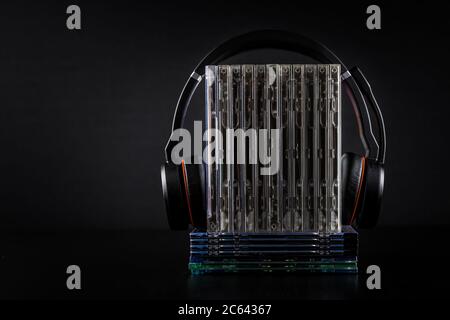 HiFi-Kopfhörer auf CD-Stapel auf schwarzem Hintergrund mit Kopierplatz.