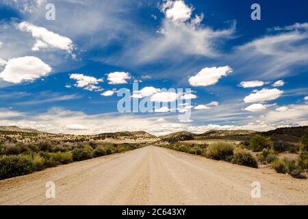 Eine alte Wüstenstraße, die in die weit reichenden Hügel hinter dem wolkenbewachsenen Himmel führt. Stockfoto