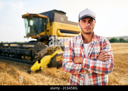 Portrait des stolzen Harvester-Maschinentreibers mit gekreuzten Händen auf der Brust. Bauer steht an seinem Mähdrescher. Agronom schaut auf die Kamera. Rancher bei Stockfoto