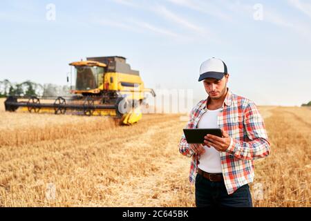 Präzisionslandwirtschaft. Landwirt hält Tablet für Mähdrescher Führung und Steuerung mit modernen Automatisierungssystem. Agronom mit Online-Daten Stockfoto