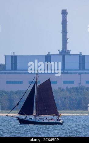 Lubmin, Deutschland. Juli 2020. Ein Segelboot segelt auf dem Greifswalder Bodden vor dem ehemaligen Gelände der 'VE Kombinat Kernkraftwerke Bruno Leuschner'. Als das Kraftwerk 1990 stillgelegt und die Bauarbeiten an den letzten beiden Blöcken eingestellt wurden, wurde auch der 126 Meter lange und 50 Meter hohe Gebäudekomplex zu einem Waisen. Der Atomhaufen in Lubmin sollte die DDR bei Stromimporten autark machen. Quelle: Jens Büttner/dpa-Zentralbild/ZB/dpa/Alamy Live News Stockfoto