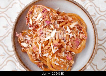 SELBSTGEMACHTER JALEBI MIT MANDELFLOCKEN UND ROSENBLÄTTERN Stockfoto