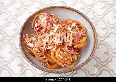 SELBSTGEMACHTER JALEBI MIT MANDELFLOCKEN UND ROSENBLÄTTERN Stockfoto