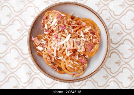 SELBSTGEMACHTER JALEBI MIT MANDELFLOCKEN UND ROSENBLÄTTERN Stockfoto