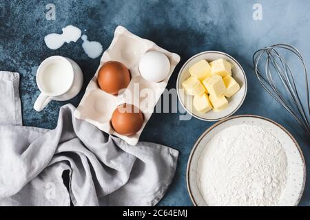 Zutaten zum Backen auf blauem Hintergrund. Eier, Butter in Würfelwürfelwürfelchen, Milchmehl und Whisker. Draufsicht Stockfoto