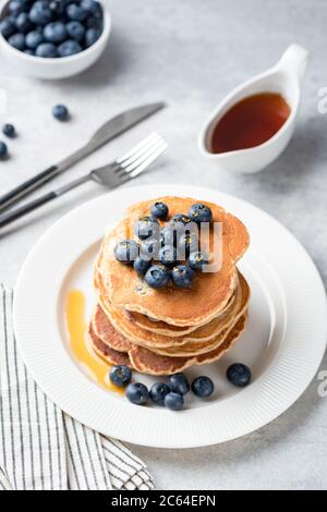 Pfannkuchen mit Heidelbeeren und Ahornsirup auf weißem Teller, grauer Betontischhintergrund. Vertikale Ausrichtung. Leckere Pfannkuchen zum Frühstück Stockfoto