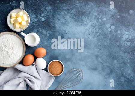 Backzutaten Mehl Eier Zucker Milch und Butter auf einem blau bemalten Hintergrund. Kopiespeicher in der Draufsicht. Backkonzept Stockfoto