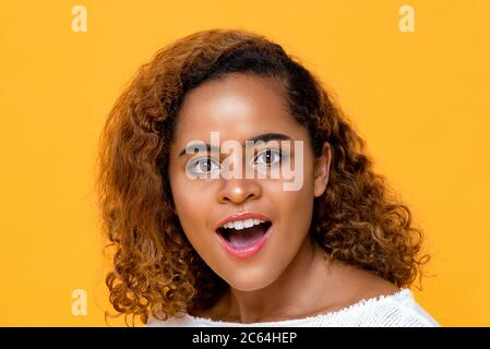 Fun Nahaufnahme Porträt von erstaunt und überrascht junge schöne afroamerikanische Frau Blick auf Kamera mit Mund offen in isolierten Studio gelb b Stockfoto