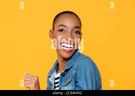 Nahaufnahme Porträt von fröhlich aufgeregt lächelnden jungen afroamerikanischen Frau mit klammernden Faust in isolierten Studio gelben Hintergrund Stockfoto