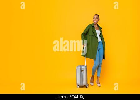 In voller Länge Porträt von Reisen glücklich junge afroamerikanische Tourist Frau stehen, während Gepäck in isolierten Studio gelben Hintergrund Stockfoto