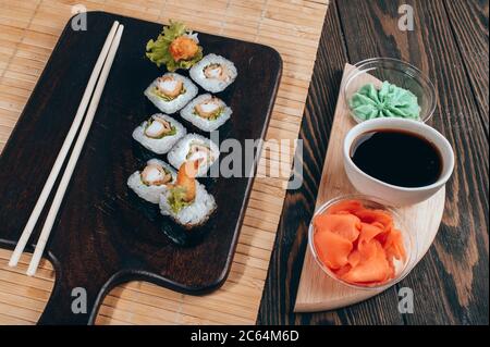 Sushi-Brötchen auf dunklem Holzbrett mit Wasabi, Sojasauce und Ingwer Stockfoto