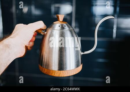 Glänzende Kaffeekanne aus Edelstahl in der Hand eines professionellen Barista Stockfoto