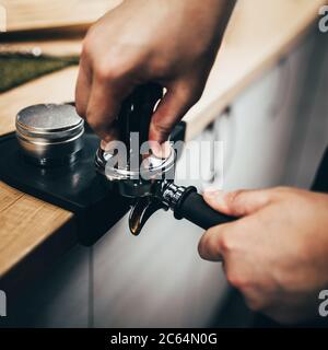Der professionelle Barista Temper presst gemahlenen Kaffee in einem Halter - Brühen in einer Kaffeemaschine Stockfoto