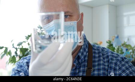 Barkeeper trägt eine Gesichtsmaske und Handschuhe in den Händen wäscht und reinigt ein leeres Glas Stockfoto