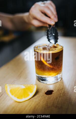 Eiskaffee europäischer Klassiker - Barista wirft Eiswürfel in ein Glas mit Zitrone Stockfoto
