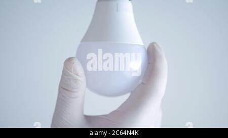 Die Hand eines Elektrikers dreht eine LED-Glühlampe in der Steckdose, um das Licht auszuschalten Stockfoto