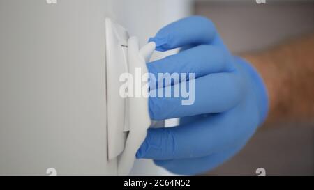 Mann trägt Schutzhandschuhe Reinigung und Desinfektion Licht Schalter aus dem Büroraum mit Desinfektionsmittel gegen Covid-19 Viren Stockfoto