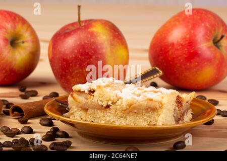 Apfelkuchen auf einem Teller mit Äpfeln, Kaffee und Zimt im Hintergrund Stockfoto