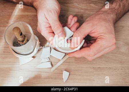 Reparatur einer geliebten Vase auf dem Boden gebrochen - Stücke von Keramik in den Händen eines Mannes - versuchen zu kleben und zu beheben Stockfoto