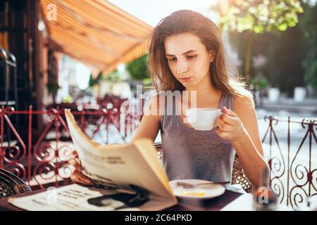 Minsk, Weißrussland - 19. Juni 2020: Junge attraktive Geschäftsfrau in Eile trinkt Morgenkaffee in einem Café, das die neueste Presse liest Stockfoto